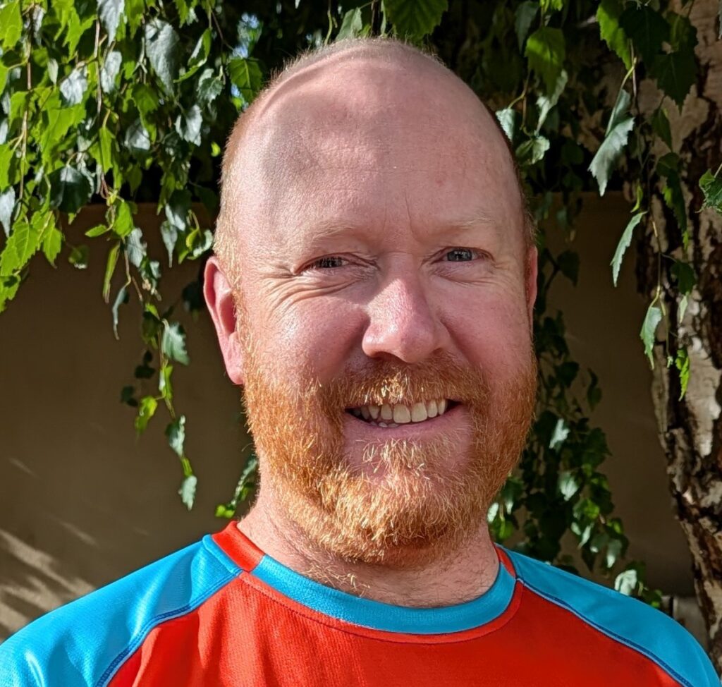 Smiling man with a ginger beard wearing a blue and orange athletic shirt